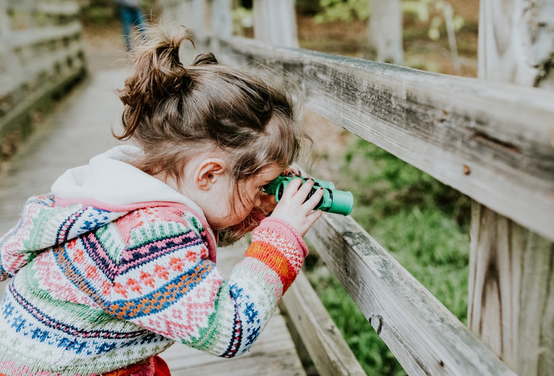 Photo by Sandra Seitamaa girl in white and red sweater leaning on brown wooden fence during daytime